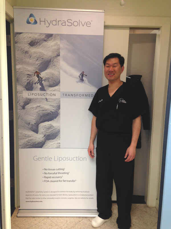 Dr. Kung standing next to a banner stand with a skier going down a snow slope. Text reads, "Gentle Liposuction."